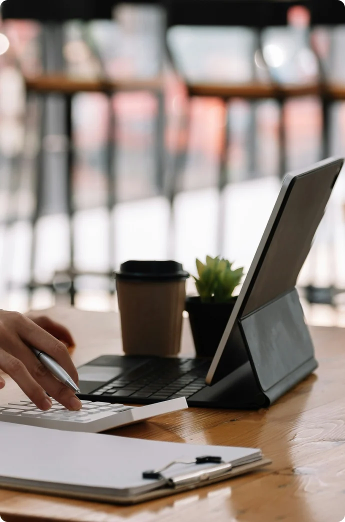 Hands typing on a laptop next to a tablet and a clipboard on a wooden desk